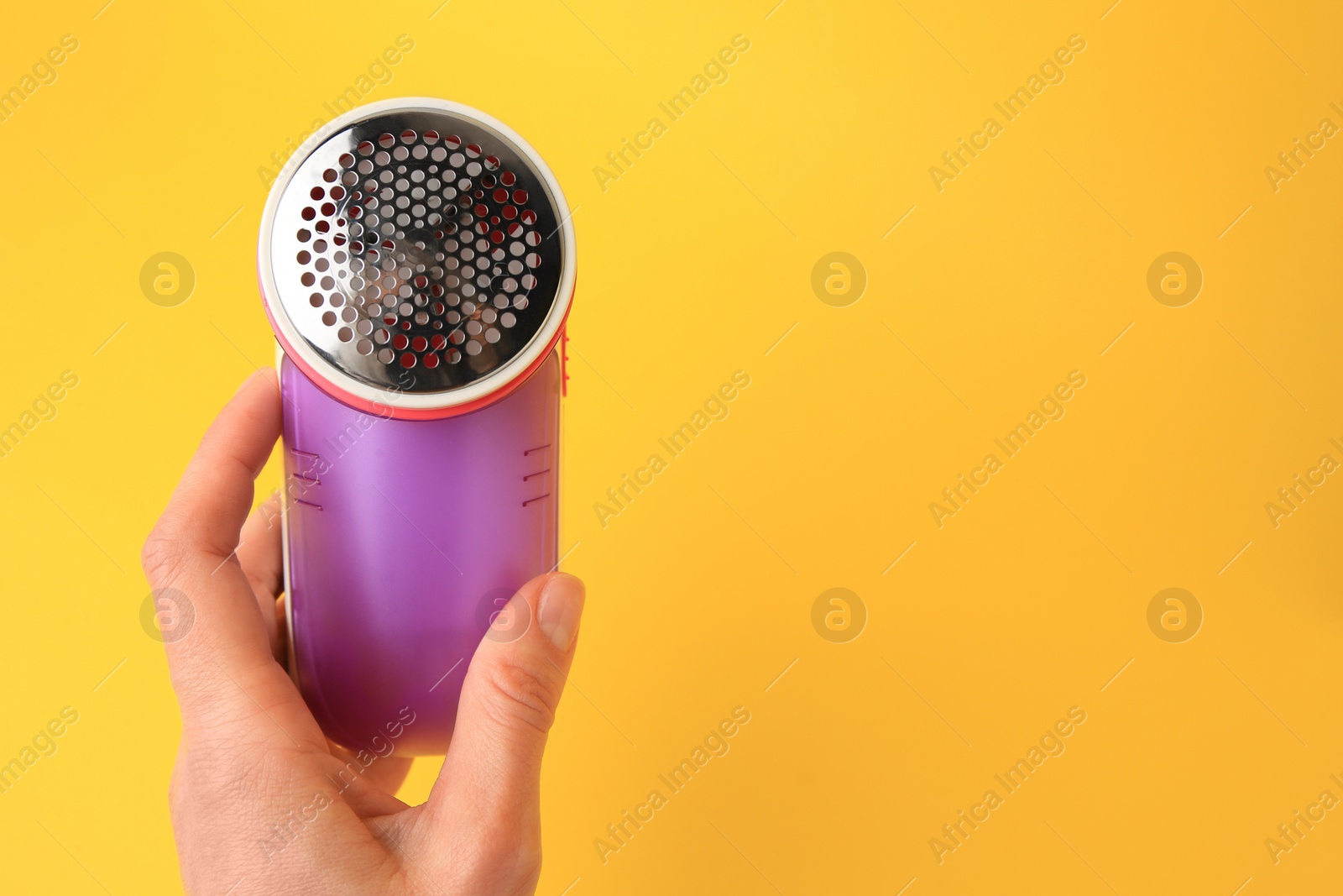 Photo of Woman holding modern fabric shaver on yellow background, closeup. Space for text