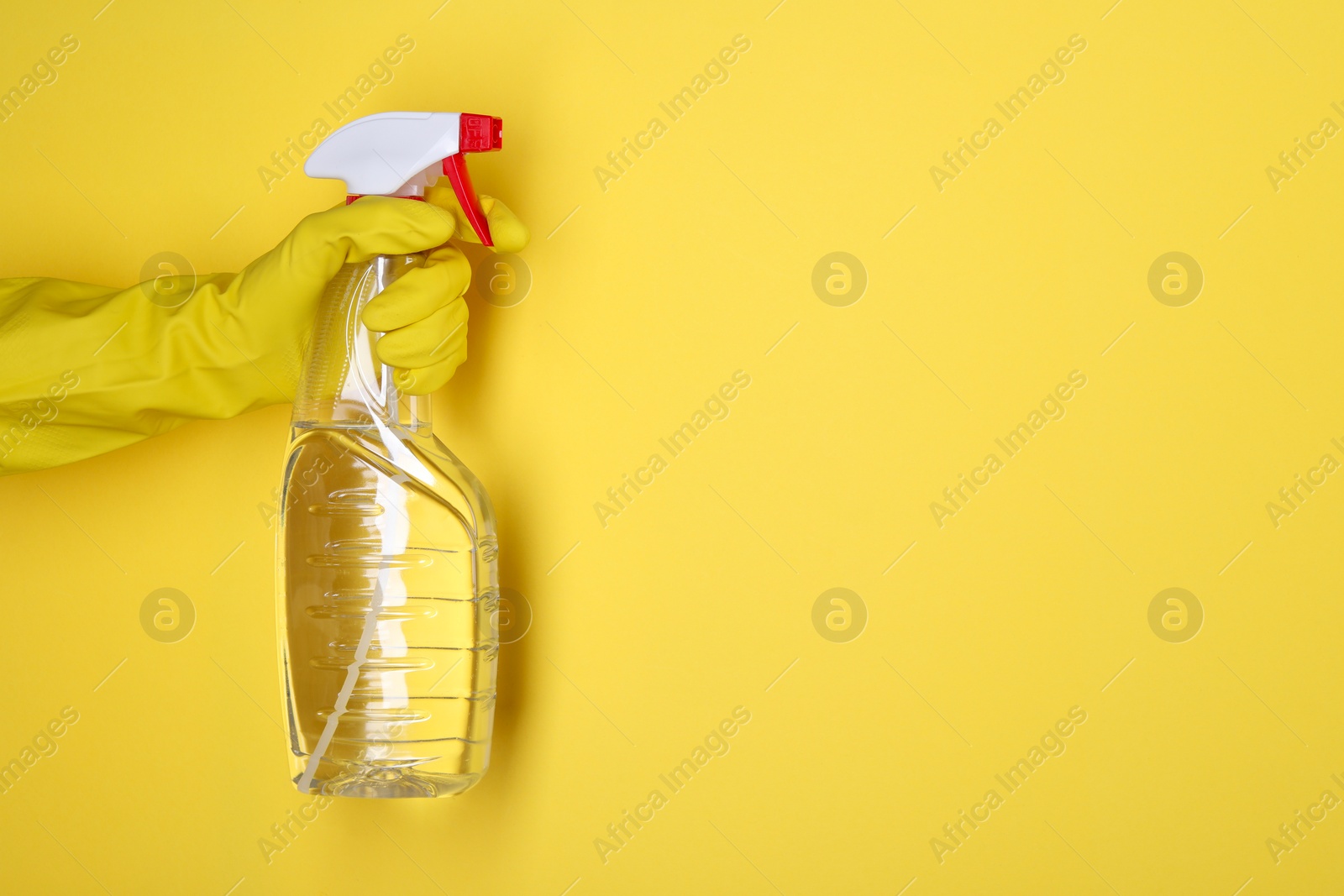 Photo of Woman holding plastic spray bottle on yellow background, closeup. Space for text