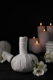 Photo of Herbal massage bags, candles, spa stones and freesia flowers on black wooden table