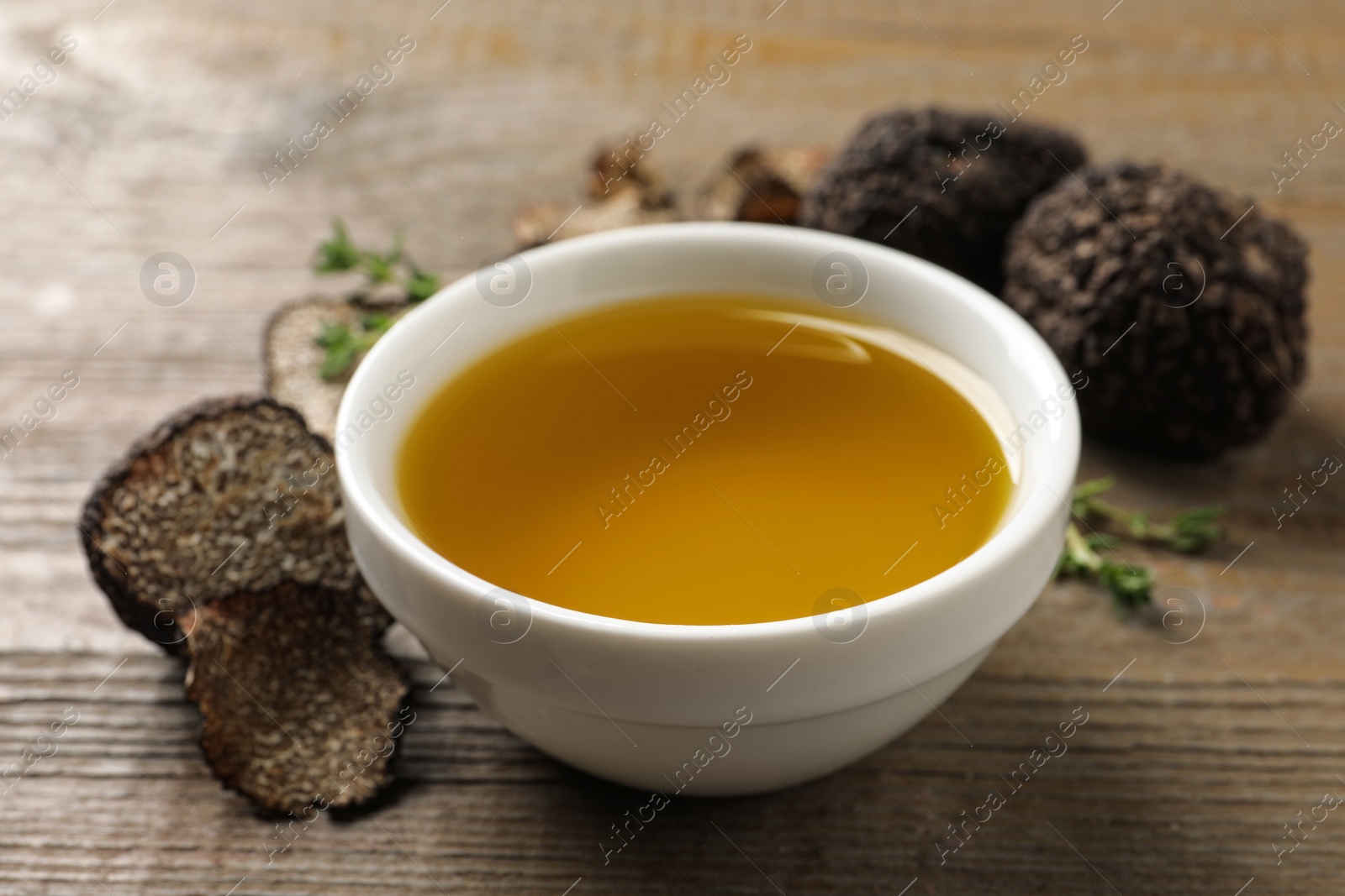 Photo of Fresh truffle oil in bowl on wooden table, closeup