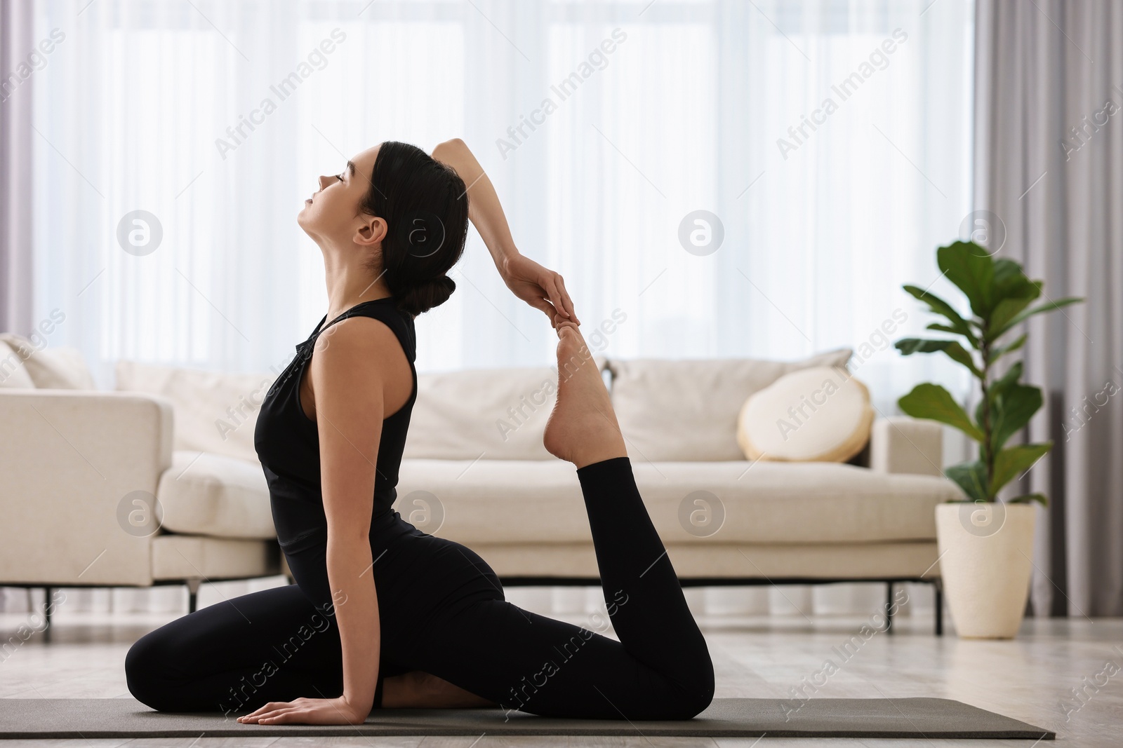 Photo of GIrl practicing one legged king pigeon asana on yoga mat at home. Eka pada rajakapotasana pose