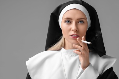 Woman in nun habit smoking cigarette on grey background. Space for text