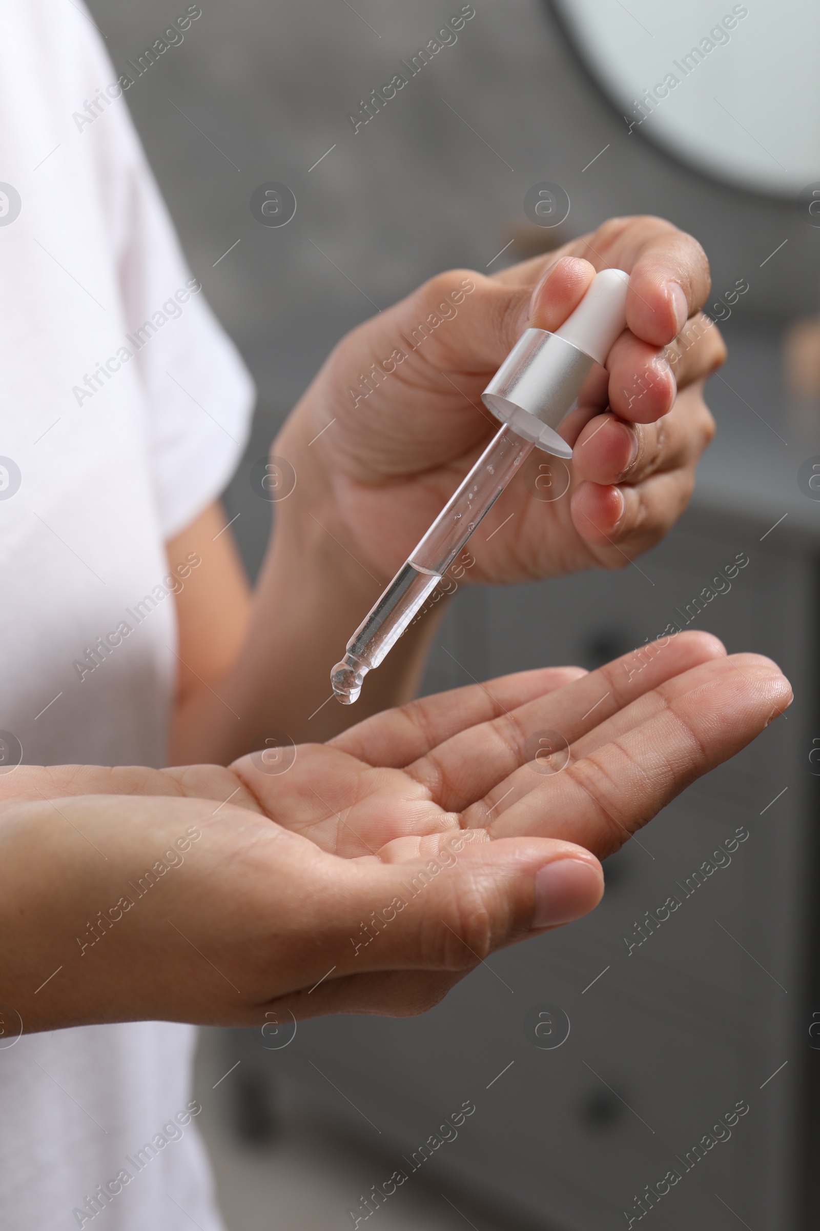 Photo of Woman applying cosmetic serum onto her hand indoors, closeup