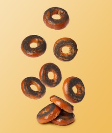 Image of Many fresh bagels with poppy seeds falling into pile on light orange background