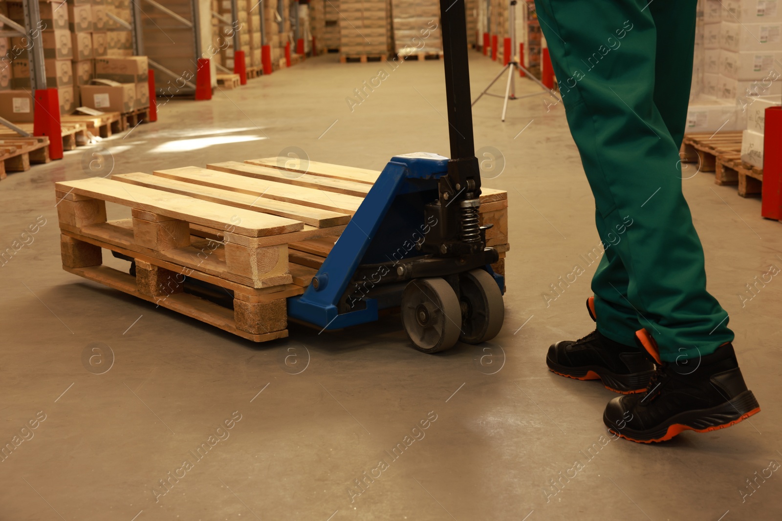 Image of Worker moving wooden pallets with manual forklift in warehouse, closeup