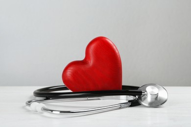 Stethoscope and red heart on white wooden table. Cardiology concept