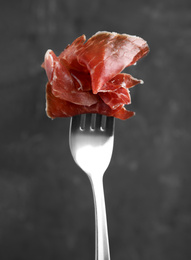 Photo of Tasty prosciutto on fork against grey background