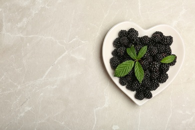 Photo of Plate of fresh blackberry and space for text on gray background, top view