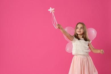 Photo of Cute little girl in fairy costume with wings and magic wand on pink background. Space for text