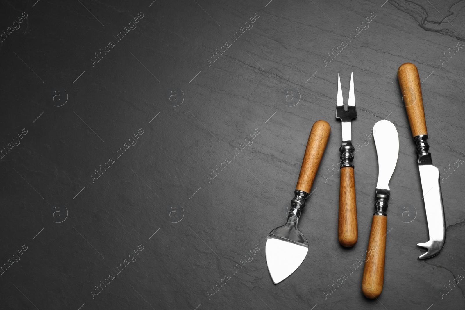 Photo of Cheese knives and fork on black stone table, flat lay. Space for text