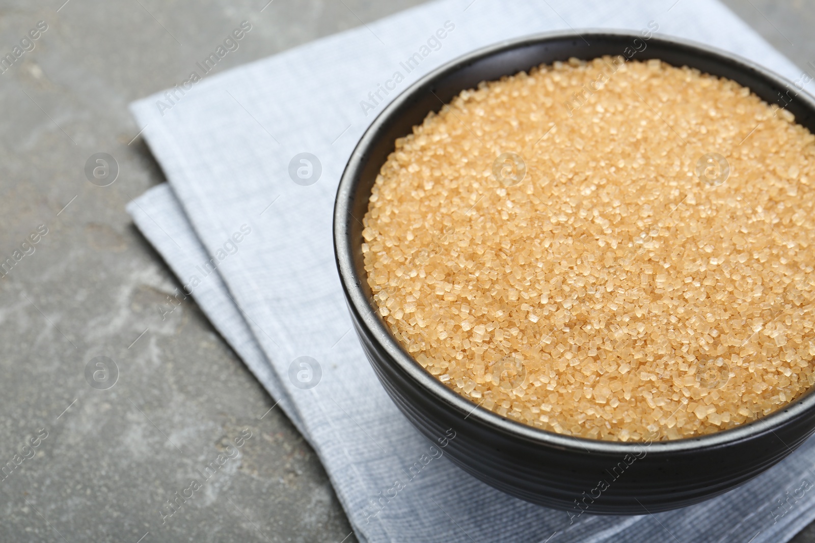 Photo of Brown sugar in bowl on grey textured table, closeup. Space for text