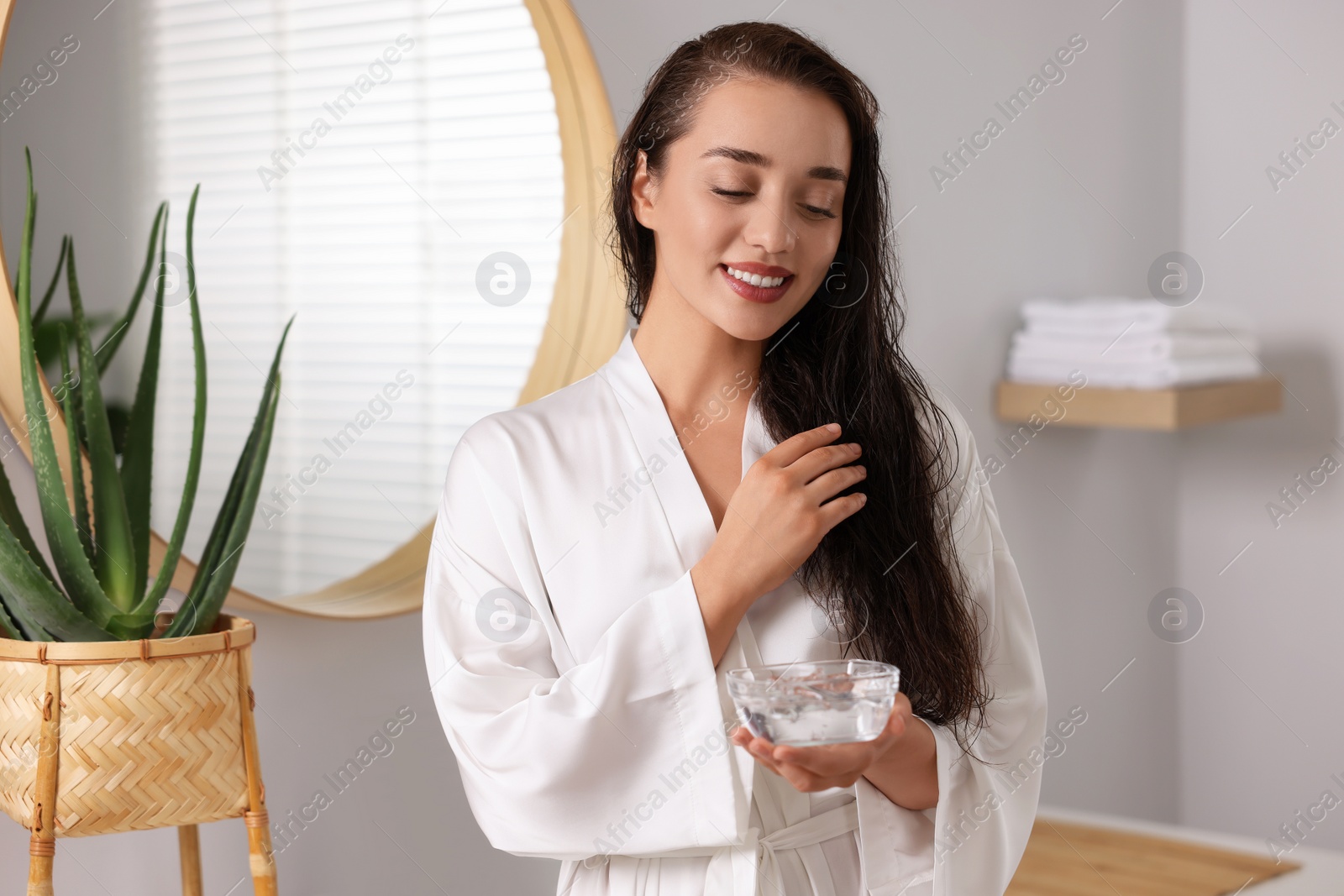 Photo of Young woman holding bowl of aloe hair mask in bathroom