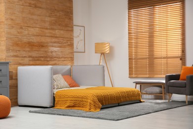 Room interior with sofa unfolded into bed near wooden wall