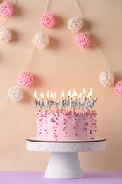 Photo of Birthday cake with burning candles on violet table