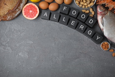 Flat lay composition of different products and black cubes with words Food Allergy on grey table, space for text