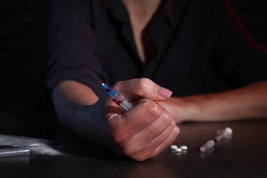 Photo of Drug addicted woman with syringe at table, closeup