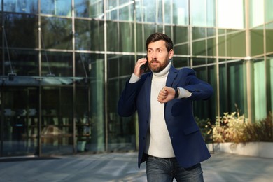 Photo of Businessman talking on smartphone and running near building. Being late concept