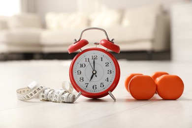 Alarm clock, measuring tape and dumbbells on wooden floor indoors. Morning exercise