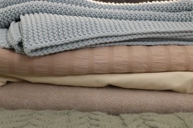 Photo of Stack of different folded blankets on bed, closeup. Home textile