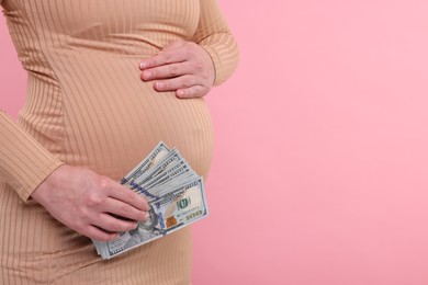 Photo of Surrogate mother. Pregnant woman with dollar banknotes on pink background, closeup. Space for text