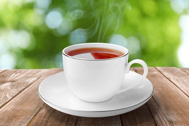 Cup of hot freshly brewed rooibos tea on wooden table outdoors