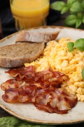 Photo of Delicious scrambled eggs with bacon and basil in plate on table, closeup