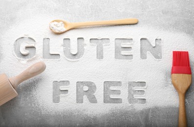 Photo of Words Gluten free written with flour and different kitchen utensils on grey background, flat lay