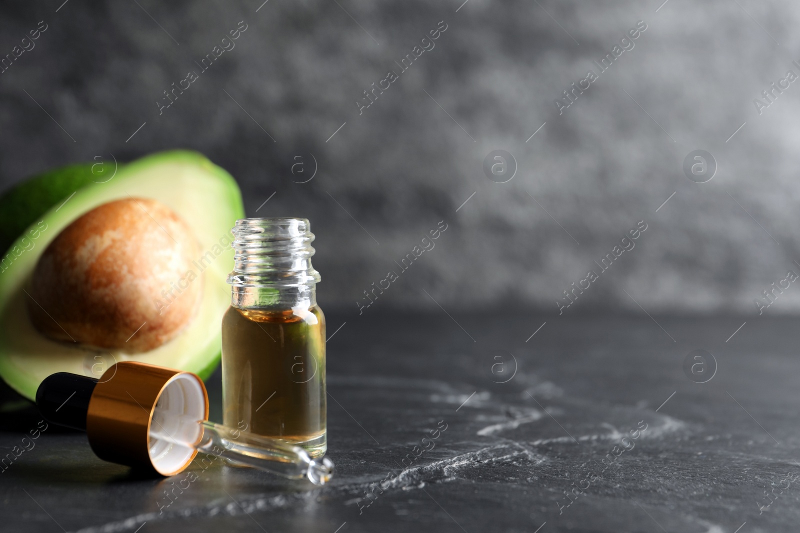 Photo of Bottle of essential oil, pipette and fresh avocado on black table, space for text