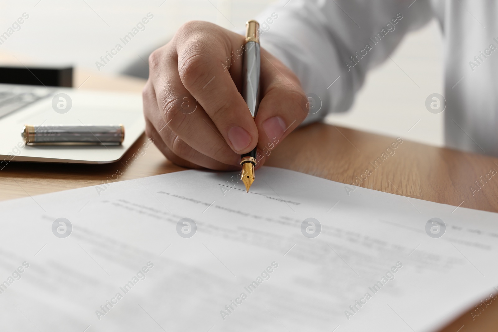 Photo of Notary signing document at wooden table, closeup