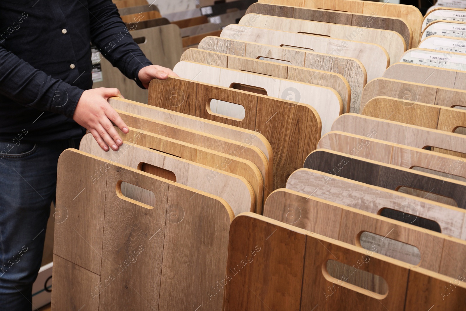 Photo of Man choosing wooden flooring among different samples in shop, closeup