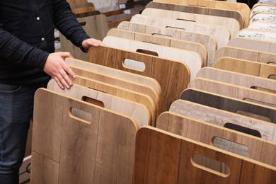 Photo of Man choosing wooden flooring among different samples in shop, closeup