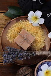 Photo of Spa composition. Sea salt, soap bar and flowers on wooden table, flat lay