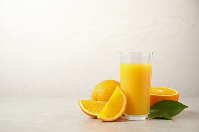 Photo of Tasty orange juice, fresh fruits and green leaves on light table. Space for text