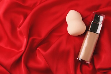 Photo of Makeup sponge and skin foundation on red cloth, flat lay. Space for text