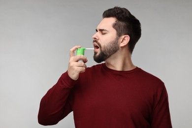 Photo of Young man using throat spray on grey background