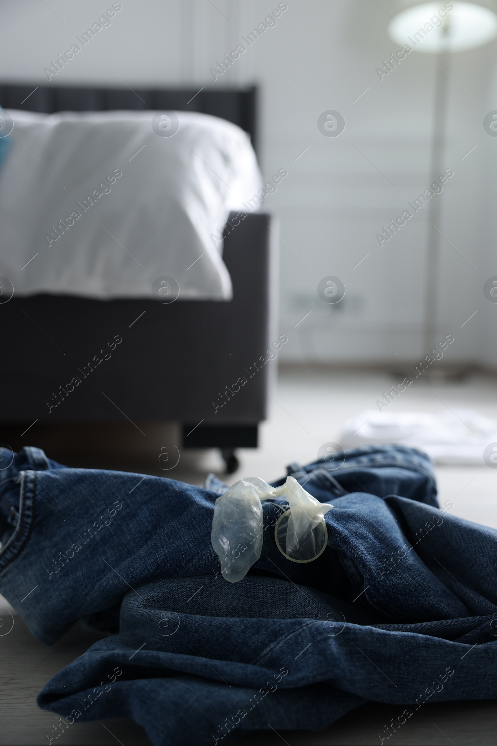 Photo of Unrolled condom and jeans on floor in bedroom. Safe sex