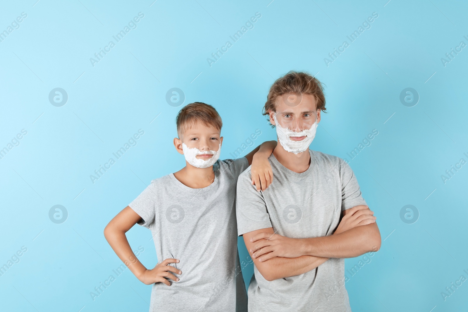 Photo of Father and son with shaving foam on faces against color background