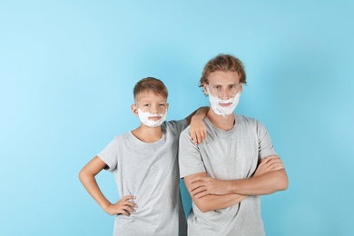 Father and son with shaving foam on faces against color background