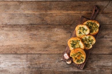 Photo of Slices of toasted bread with garlic and herbs on wooden table, top view. Space for text