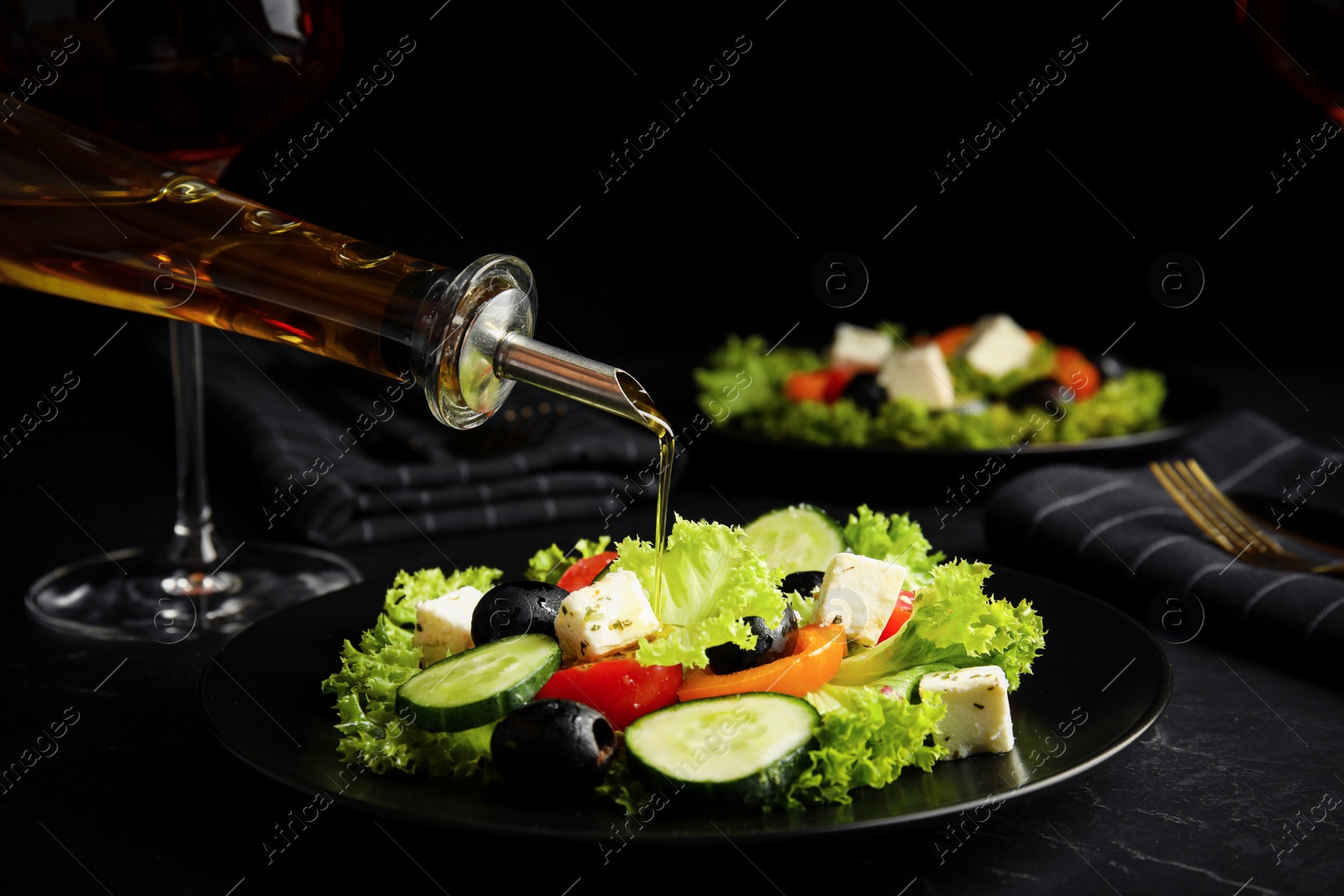 Photo of Dressing tasty fresh Greek salad with olive oil on dark table