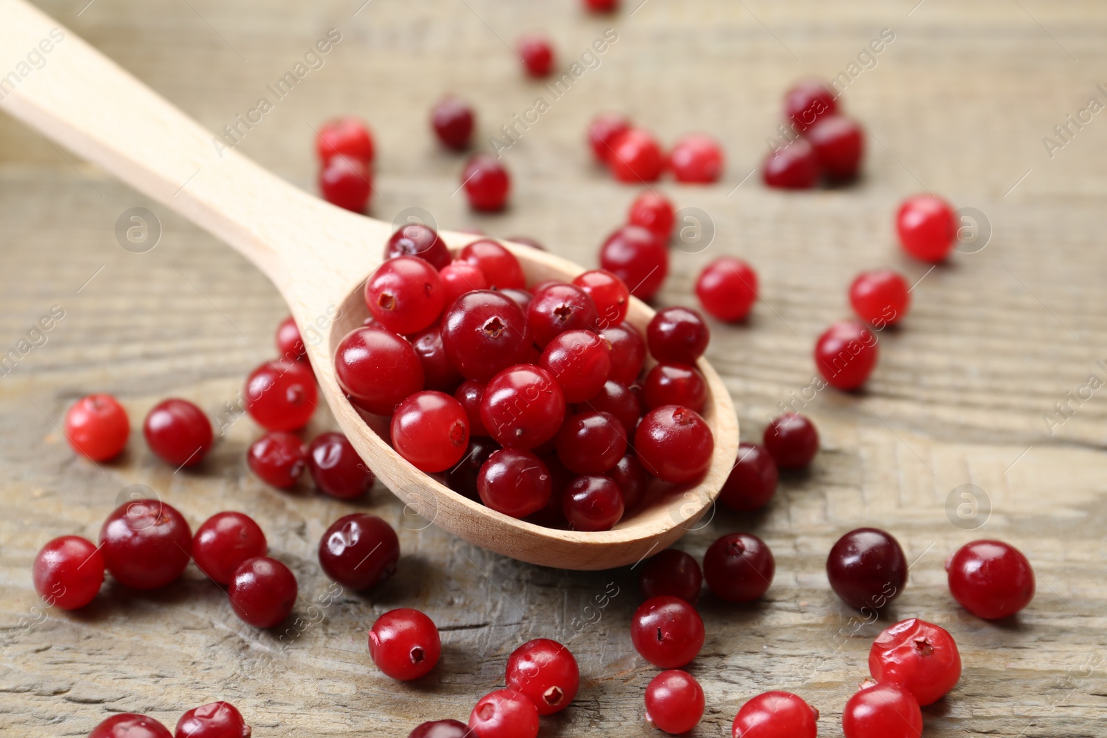 Photo of Spoon with fresh ripe cranberries on wooden table, closeup