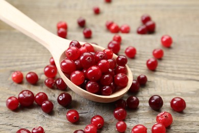 Photo of Spoon with fresh ripe cranberries on wooden table, closeup