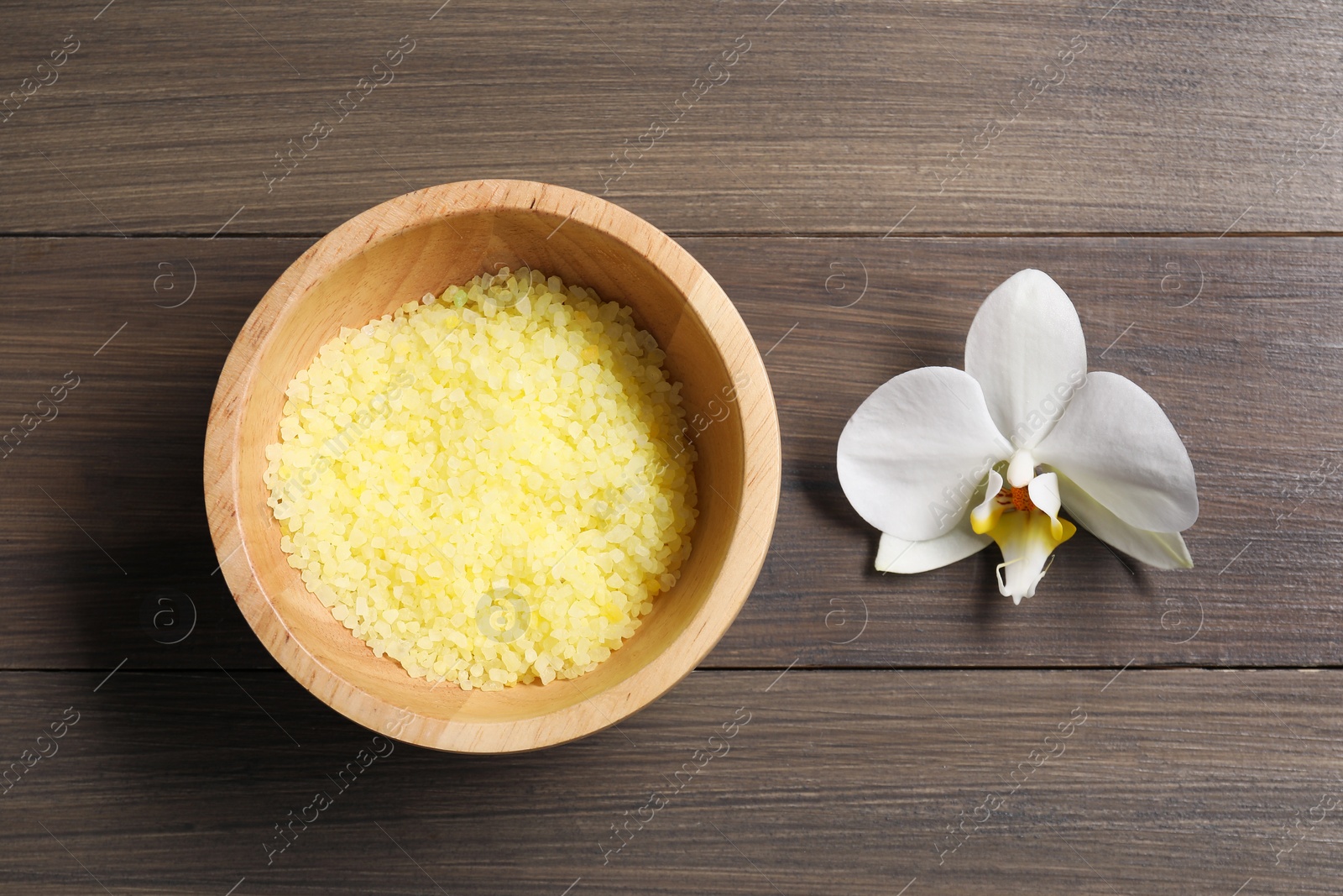 Photo of Natural sea salt in bowl and beautiful orchid on wooden table, top view