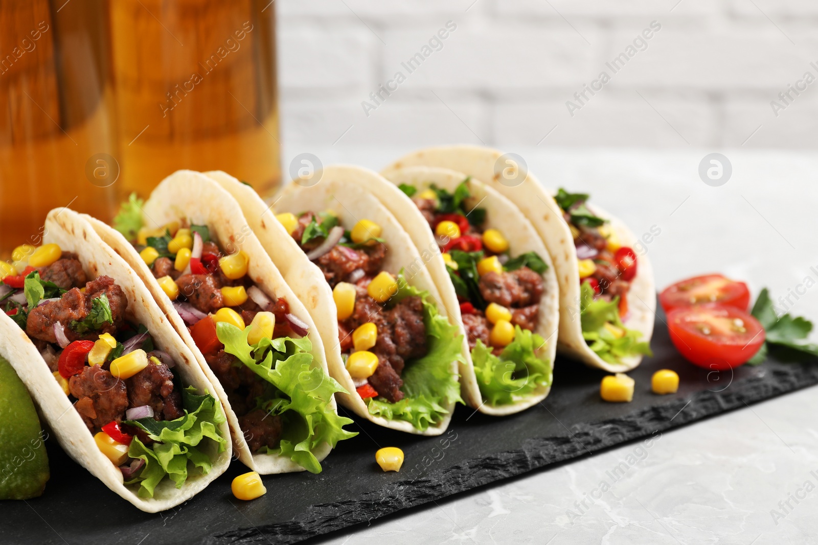 Photo of Delicious tacos with meat and vegetables on light gray marble table, closeup