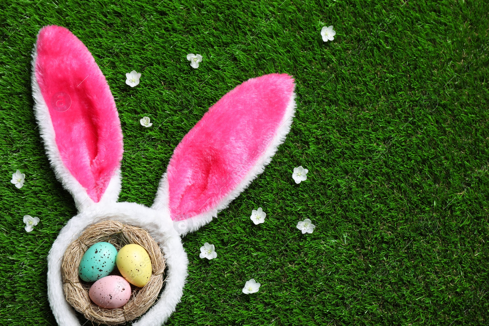 Photo of Flat lay composition with decorative bunny ears and painted eggs on green grass, space for text. Easter holiday