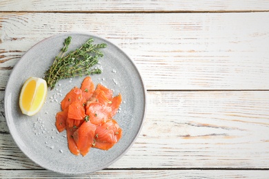 Photo of Plate with fresh sliced salmon fillet, lemon and thyme on wooden background, top view