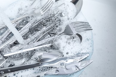Photo of Washing silver spoons, forks and knives under stream of water, above view