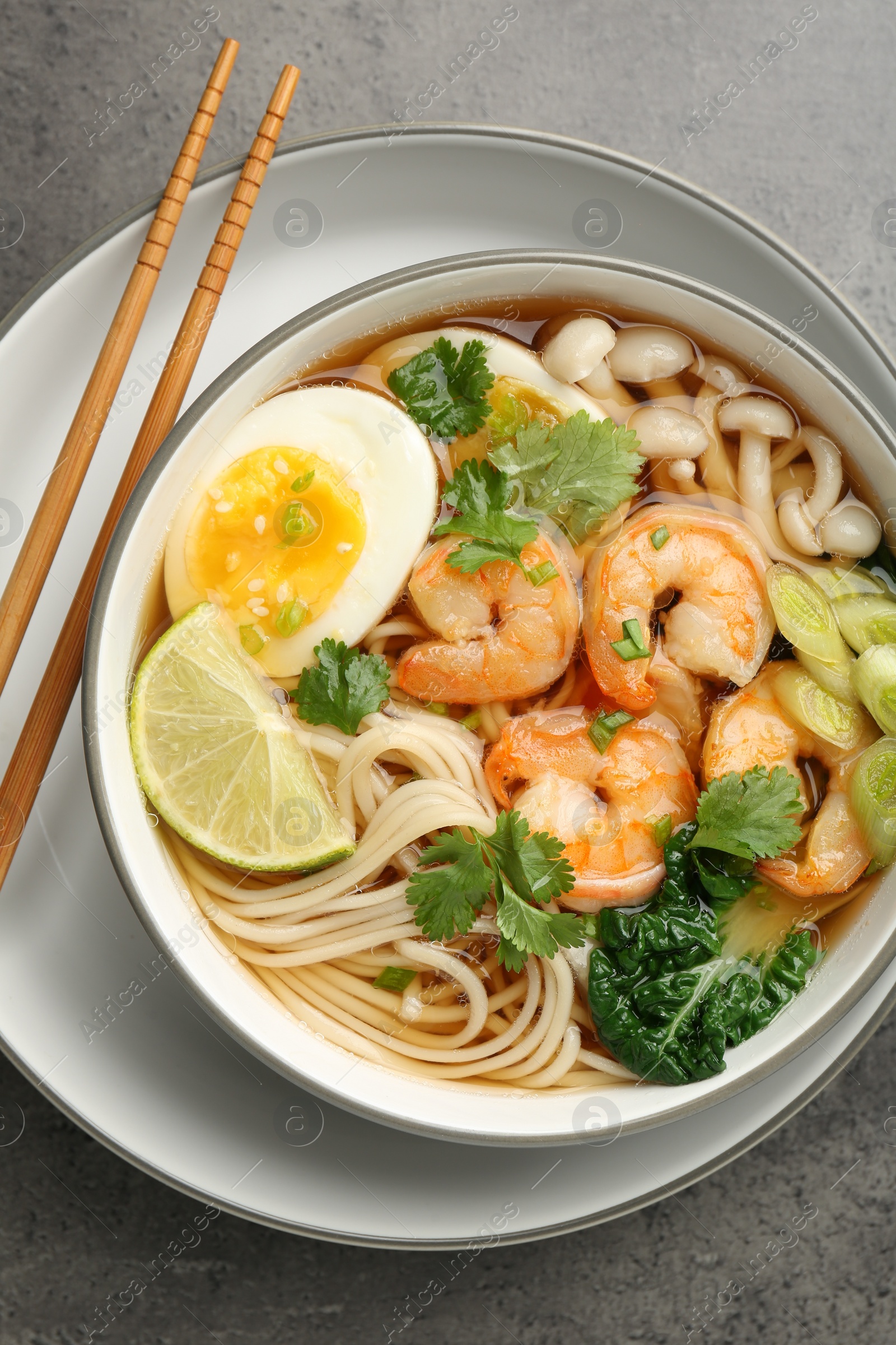 Photo of Delicious ramen with shrimps and chopsticks on grey table, top view. Noodle soup