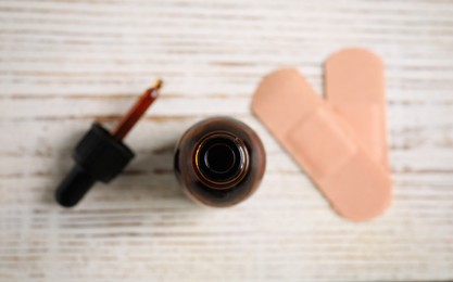 Bottle of medical iodine, dropper and sticking plasters on white wooden table, flat lay