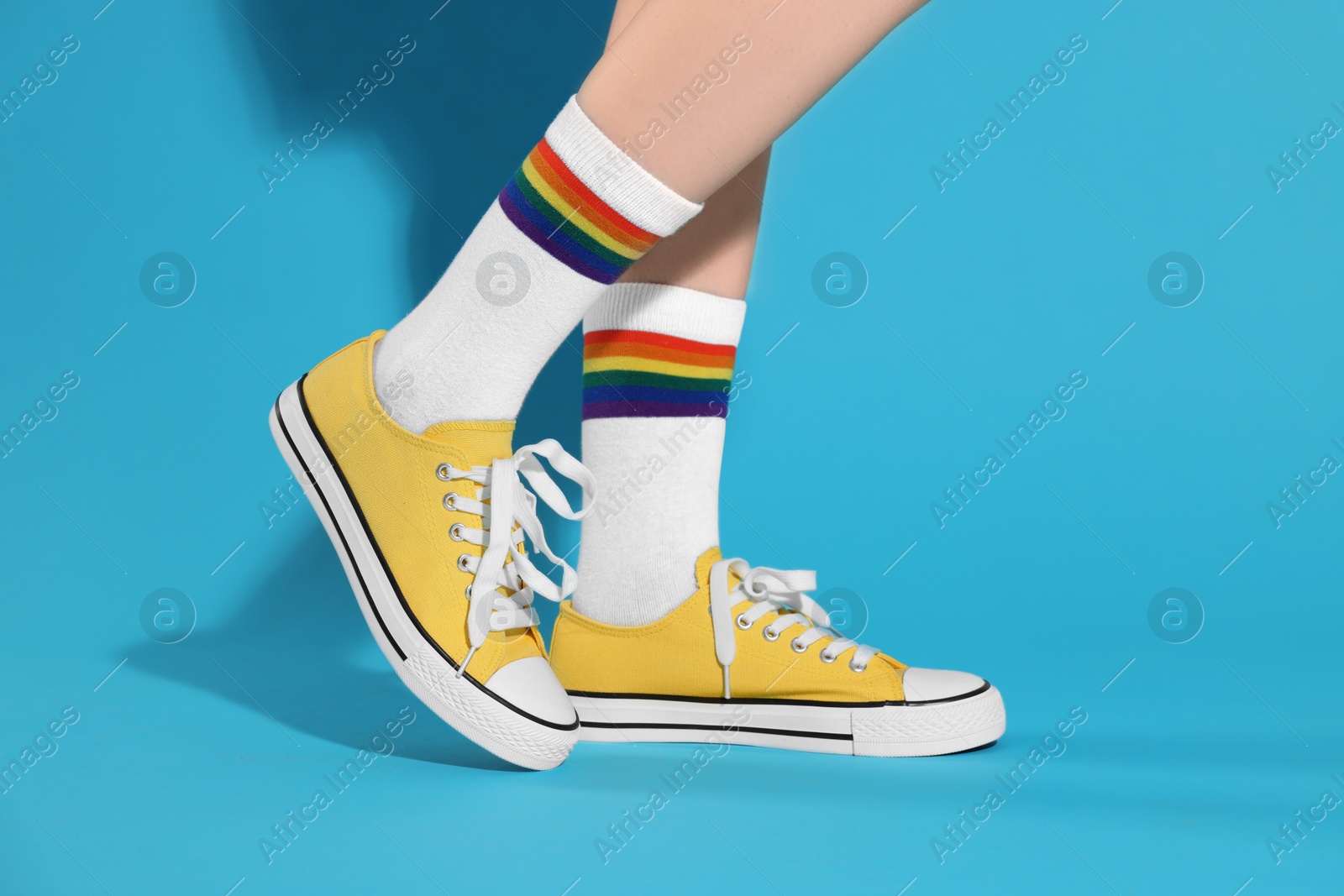 Photo of Woman wearing yellow classic old school sneakers on light blue background, closeup